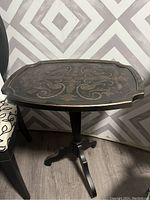 Side view of black wooden side table with painted decorative top and pedestal base