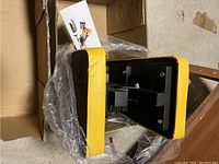 Photo showing the yellow and black padded weight bench in a folded state inside a cardboard box.