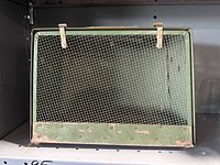 Front view showing wire mesh door with two strap fasteners on top and metal frame.