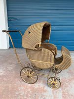 Side view of antique wicker baby stroller with hood, metal frame, and wooden handle ends.