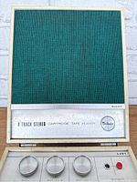 Closed view of green mesh speaker cover on the right side with nameplate labeling 8 Track Stereo Cartridge Tape Player and Belair logo.