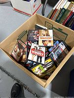 Box containing over 50 DVDs visible with titles from various movies and genres, cases stacked inside a cardboard box.