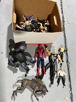 Box of toy action figures with larger figures placed in front including King Kong, Spider-Man, skeletal warrior, canine creature, and a small beige figure.