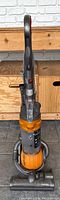 Front view of Dyson upright vacuum cleaner showing clear dust bin with orange and gray body