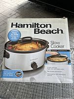 Front view of the Hamilton Beach slow cooker in its original box showing product image and features.