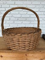 Side view of a large round wicker basket with an arched handle, showing worn natural brown wicker material.