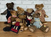 Group of nine Boyd's Bears large plush toys in various outfits on wooden floor against white brick wall.