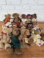 Front view of the lot showing approximately 20 Boyd's Bears plush toys with various outfits and sizes on wood floor against white brick wall background.