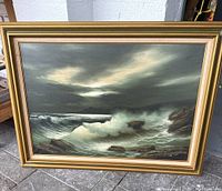 Framed oil painting of an ocean scene showing waves crashing against rocks under a moody sky.