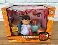 Front view of Peanuts Lucy Halloween party playset in box showing Lucy figurine, TV, pumpkin, and background decorations.