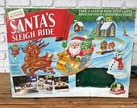 Box of the Santa's Sleigh Ride Christmas decoration set showing front artwork with Santa, reindeer, elves, snowman, and snow-covered buildings