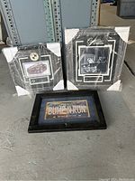 Three pictures, two wrapped with corner protectors, on the floor showing Cadillac themed framed photos and a sign.