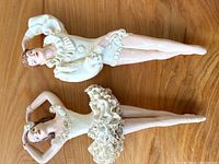 Two vintage dancing figures displayed on wood surface, both posed with arms overhead and wearing detailed dance costumes.