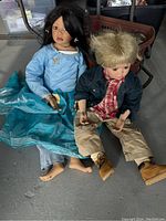 Two large ceramic dolls approximately 34 inches tall, seated on the ground, showing clothing and overall condition.