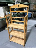 Wooden upright folding shelf with three shelves, side slats, and a rounded top back panel in a warehouse setting.