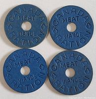 Four blue Canadian meat ration tokens with central holes, circular and stamped with 'CANADA MEAT RATION' and 'VIANDE RATION' with maple leaf symbols.