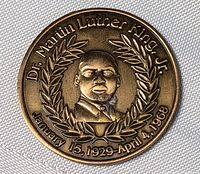 Front side of bronze-colored medallion coin showing Dr. Martin Luther King Jr. profile with laurel and dates.