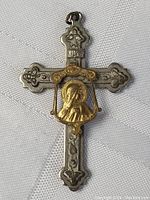 Front view of vintage metal religious cross pendant with gold saint relief on white fabric background.