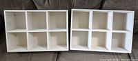 Two white wooden display shelves each with six compartments arranged in 3x2 layout, shown together on a couch.