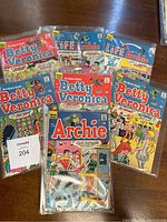 Seven sleeved Archie comics laid out on wooden surface including multiple Betty and Veronica issues, Life with Archie, and one titled Archie.