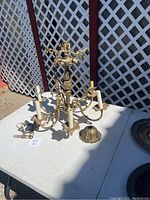 Brass chandelier displayed on a table outdoors, showing the overall condition and shape of the fixture, including the hanging chain and canopy.