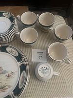 Partial Kelcraft by Noritake Ireland china set displayed on a cloth surface showing cups, saucers, and plates with distinctive hunting scene pattern and green borders.