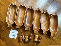 Six wooden corn cob shaped serving dishes with grooves and notch ends, medium-tone polished wood surface.