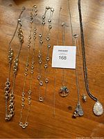 Full view of all 8 necklaces laid flat on a wooden surface showing various chain styles and pendants