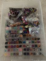 Plastic containers and bags filled with colorful sequins and confetti in various shapes and colors, arranged on a surface.