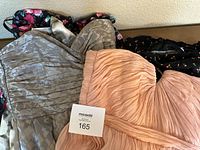 Cluster of dresses lying on wooden surface, including a peach strapless dress, gray textured dress, and floral prints