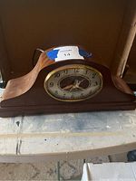 Side view of the wooden mantel clock showing the curved wooden case with a slot for the clock face and a power cord at the back.