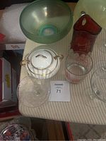 Photo showing a pearlescent green decorative glass bowl, white and gold-trimmed stemware, red commemorative glass pitcher from the 1967 World's Fair, and two clear glass mugs with red McDonald's logos and markings.