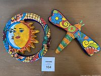 Overview of Mexican pottery sun and dragonfly pieces on a wooden surface.