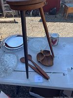 Wooden bowl, two wooden salad utensils, a three-compartment wooden serving dish, and part of the three-legged wooden lazy Susan, along with glass plates and a silver tray on an outdoor table