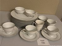 Photo showing stacked white china plates with gold or silver rims, cups and saucers arranged on table.