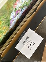 Close up photo showing damage on the black and gold frame of one painting and some scratches on the painting surface.