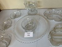 Full view of all 8 glass pieces in the lot arranged on a white surface showing the variety of shapes and styles including plates, bowled, and candle holder.