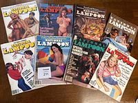 Top view of 8 vintage National Lampoon magazines fanned out on wood surface showing varied cover art and wear.