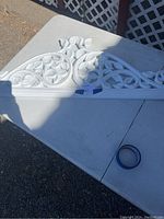 Two white carved wooden wall hanging pieces placed on a white surface outdoors, showing intricate scroll and floral designs.