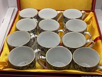 Set of 12 vintage Chinese teacups arranged in original box with yellow satin interior.