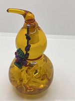 Front view of amber colored glass gourd bottle showing bulbous shape, cork stopper, brown cord with green and purple beads