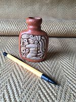 Front view of the small clay bottle showing one side with detailed relief carving of a Mayan figure.