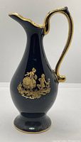 Front view of a tall Limoges porcelain pitcher featuring a deep blue body and a gold depiction of a woman and child, gold trim on the base, rim, and handle.