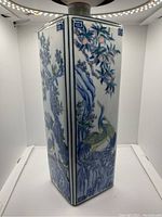 Front corner view showing detailed painting of yellow and blue birds with flowering trees and rocks on a square porcelain vase.