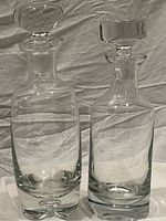 Two clear antique crystal decanters side by side on a white cloth background.