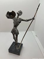 Full front view of the Don Quixote sculpture showing figure holding shield and spear on marble base.