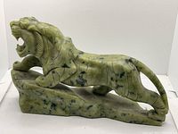 Side view of hand-carved green jade tiger statue on a jade base showing the crouching pose and body details.