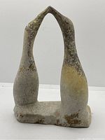 Front view of the hand carved stone sculpture showing two elongated birds with necks touching at the beaks forming a kissing pose in beige and brown tones.