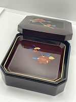 Inside of the lacquerware box showing one of six matching lacquerware style plates with floral design and gold trim