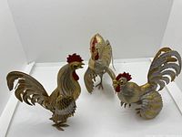 Three metallic chicken figurines in gold and silver tones with red ruby accents, showing condition and poseable wings